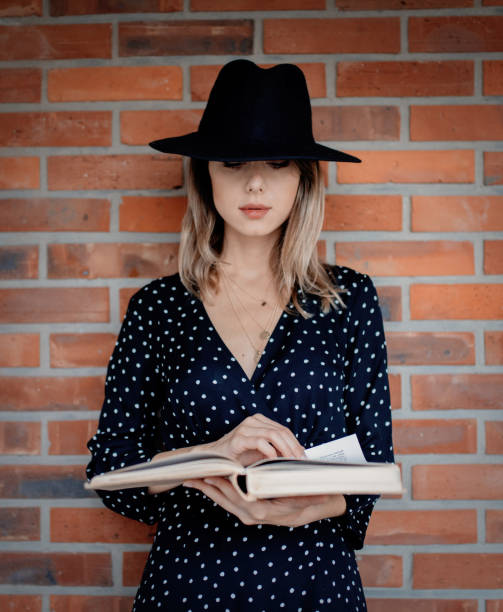 istock woman in hat with book on brick wall background 1163409508