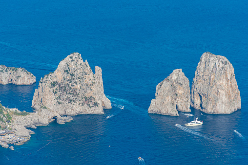 High angle view of the Faraglioni, located in the of the Island of Capri in the Tyrrhenian Sea in Italy. Boats are floating in front of them, This are rock formations eroded by the wind and water.