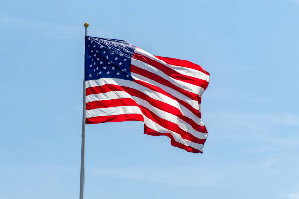 American flag waving on pole with bright vibrant red white and blue colors against blue sky American flag waving on pole with bright vibrant red white and blue colors, negative space pole stock pictures, royalty-free photos & images