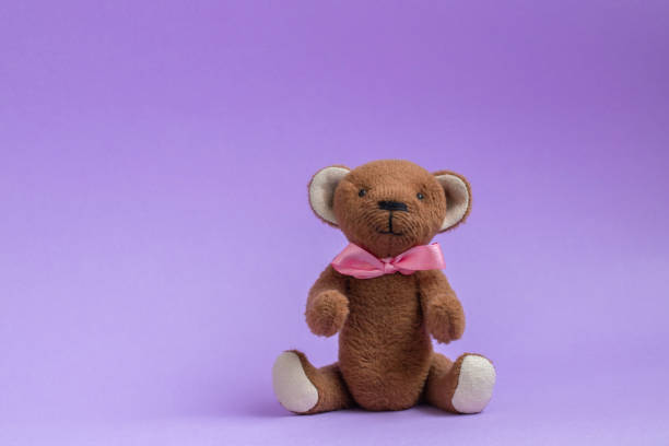 Teddy bear sitting on purple background. Teddy bear toy with pink bow. Copy space, postcard. Plush toy handmade.