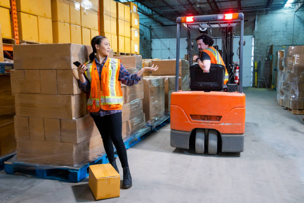 istock An industrial warehouse workplace safety topic. A female worker distracted by her mobile cell phone as a forklift approaches. 1163426910