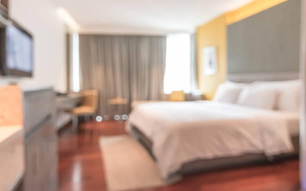 istock Hotel bedroom blur background guest room interior with blurry comfortable king size bed white, bedsheet, TV, work table desk and chair furniture 1163428028