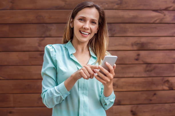 istock Young woman in blouse standing isolated on wall browsing smartphone looking camera cheerful 1163429411