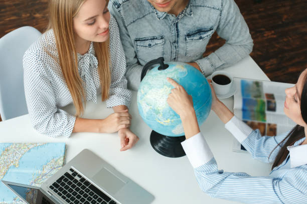 Young couple in a tour agency communication with a travel agent travelling concept destination on a globe stock photo