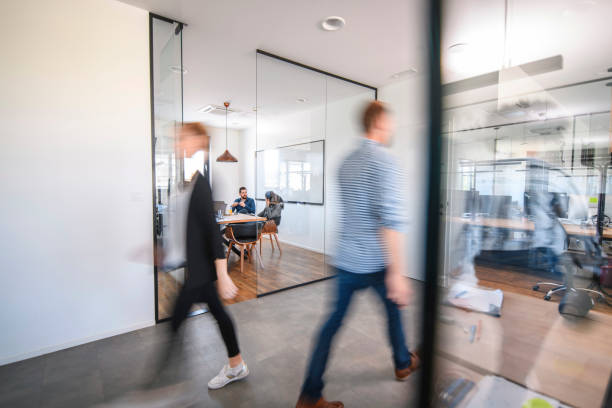 Business Colleagues in Motion Past Office Conference Room Blurred motion of male and female businesspeople walking down hallway contrasted by still and careful debate of new ideas in the conference room. business relationship photos stock pictures, royalty-free photos & images