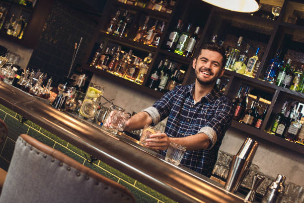 istock Young bartender standing at bar counter holding cocktails smiling cheerful 1163429632