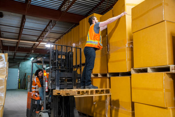 istock An industrial warehouse workplace safety topic. A dangerous situation as a worker is lifted-up by a forklift to reach higher placed merchandise. 1163430461