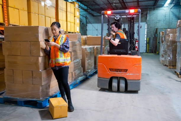 istock An industrial warehouse workplace safety topic. A female worker distracted by her mobile cell phone as a forklift approaches. 1163430534