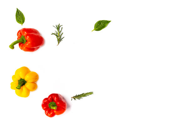 Colorful yellow, red, and orange bell peppers with rosemary sprigs and basil leaves on white background.  Top view.