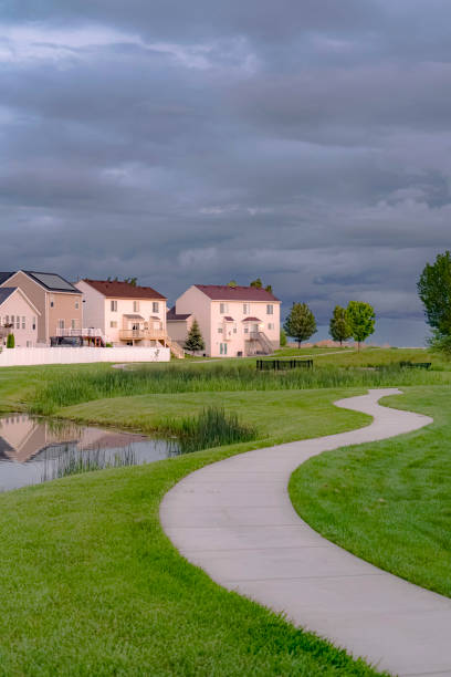 istock Neighborhood park with pond bridge and pathway under sky with thick gray clouds 1163437591