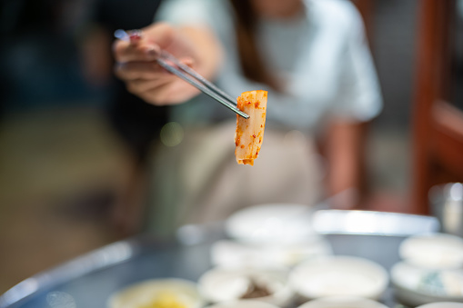 Young woman holding a piece of kimchi with Korean metal chopsticks