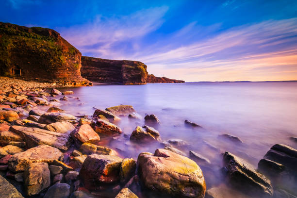 Images shows a low sunset grazing the top of the horizon with waves crashing along the shore in the fore ground.