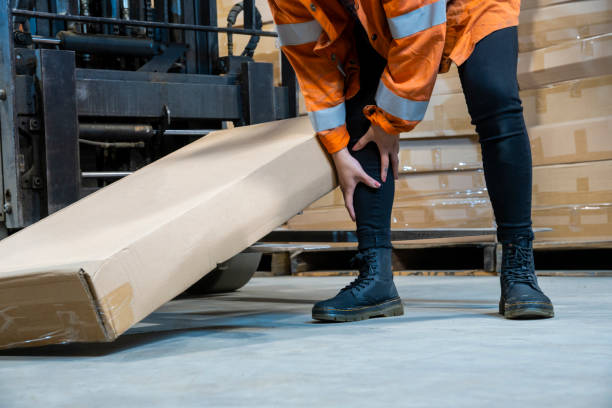 Un argomento sulla sicurezza sul posto di lavoro del magazzino industriale.  Un'impiegata ferita dall'inciampo sulle forchette del carrello elevatore. - foto stock