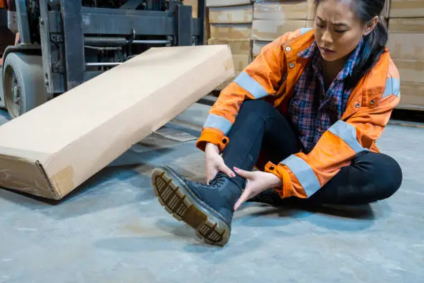 An industrial warehouse workplace safety topic.  A female employee injured by tripping over forklift forks.  Forks must be placed on the ground to avoid being trip hazards.