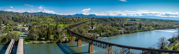 Aerial panorama of Redding, California, looking across the Sacramento River where it is crossed by a road bridge, a rail bridge and the Sacramento River Trail