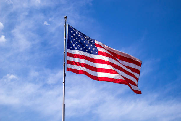 istock United States flag on a pole waving on blue sky background. 1163458814