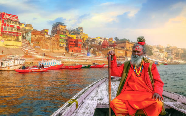 Indian sadhu (monk) enjoy boat ride at Varanasi Ganges river with view of ancient Varanasi city architecture and ghat Sadhu baba sitting on a wooden boat overlooking ancient Varanasi city architecture with Ganges river ghat at sunset. ghat photos stock pictures, royalty-free photos & images
