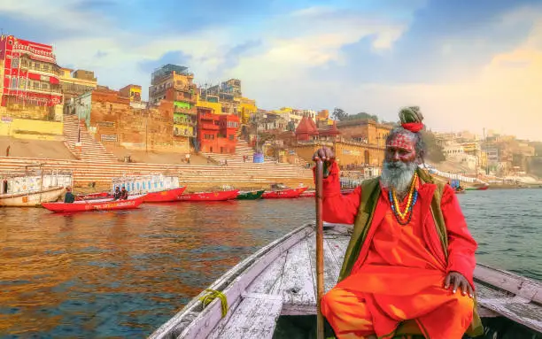 Photo of Indian sadhu (monk) enjoy boat ride at Varanasi Ganges river with view of ancient Varanasi city architecture and ghat