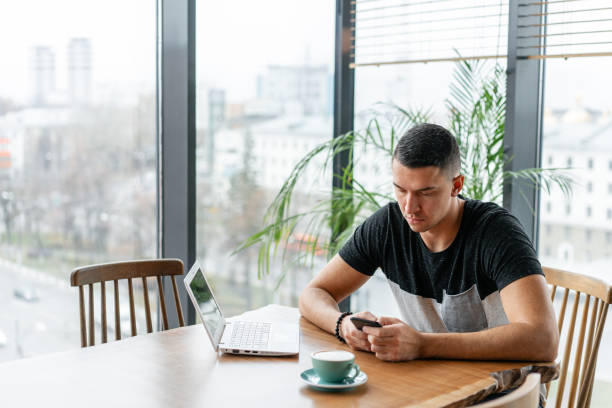 istock Freelancer work on netbook in modern coworking. Young man drinking coffee from a Cup. Programmer at remote job. Successful people, businessman in comfortable cafe. High large Windows 1163467270