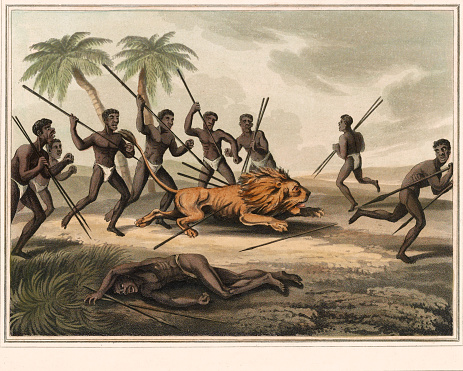Vintage illustration features Native Africans with spears surrounding a lion. An injured man lies in the foreground.