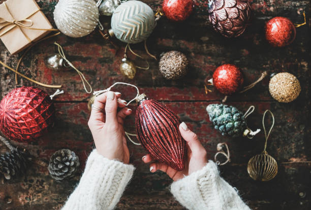 Christmas decoration toys and woman's hands over rustic wooden background Christmas or New Year holiday background, texture, wallpaper. Flat-lay of Christmas festive decoration toys and wonan's hands holding red toy over red rustic wooden background, top view christmas human hand christmas ornament decoration stock pictures, royalty-free photos & images