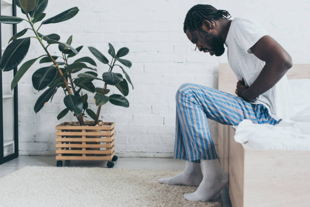 istock young african american man suffering from stomach ache while sitting on bed 1163476995