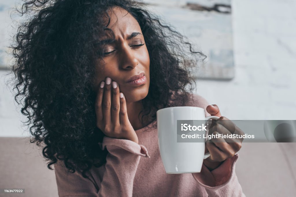 femme américaine africaine malheureuse souffrant de mal de dents et retenant la tasse de café - Photo de Rage de dents libre de droits