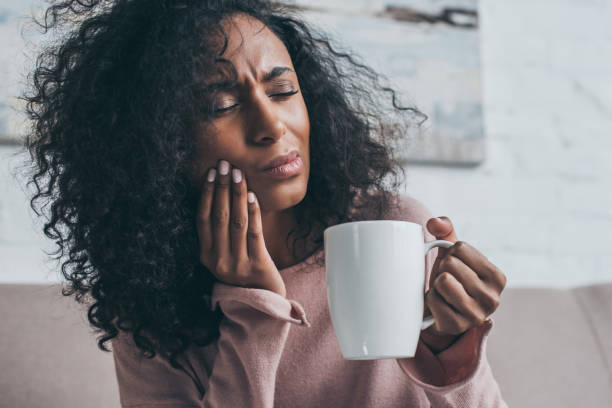 歯痛に苦しんでコーヒーカップを持っている不幸なアフリカ系アメリカ人女性 - 歯痛 写真 ストックフォトと画像