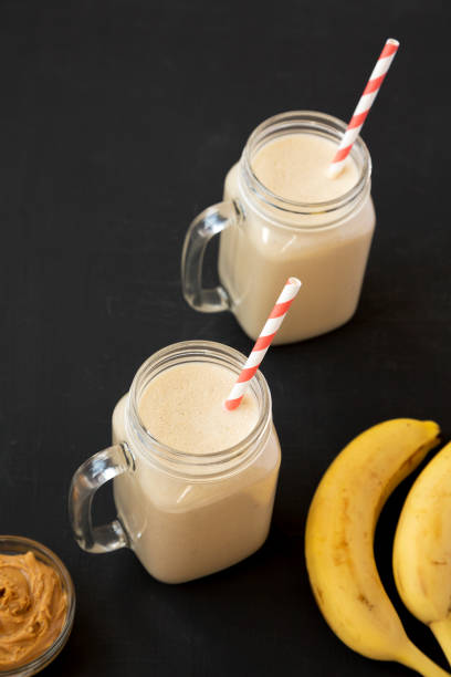 Mason glass jar mugs filled with peanut butter banana smoothie on a black background, low angle view. Copy space.