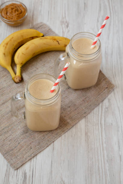 Peanut butter banana smoothie in glass jars on a white wooden background, low angle view. Close-up.