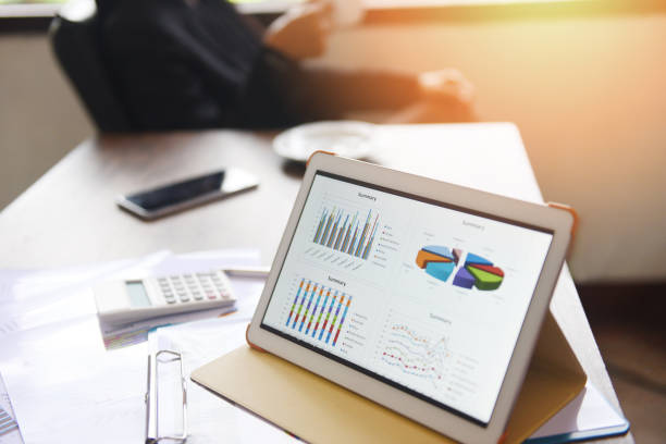 istock Business graphs chart on a tablet computer technology on the table and woman working in office with coffee cup - sale report money analyzing 1163479561