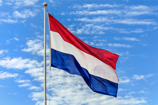 The national flags of the Netherland flag on the background of blue sky with clouds.