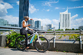 sporty businesswoman on e bike with mobile phone outdoors office buildings background