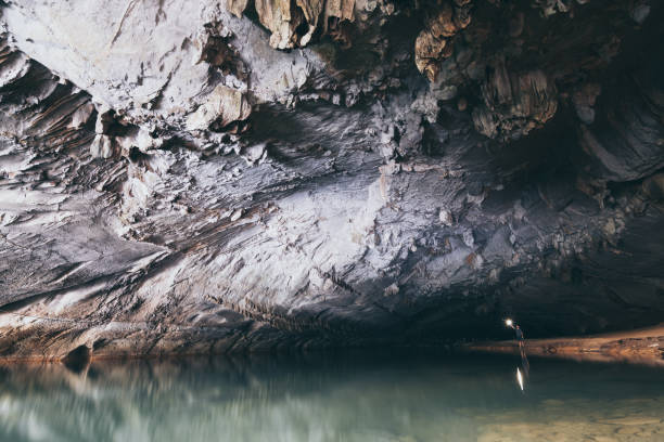istock Human silhouette stands inside water cave with torch in hand in Konglor, Laos 1163489520