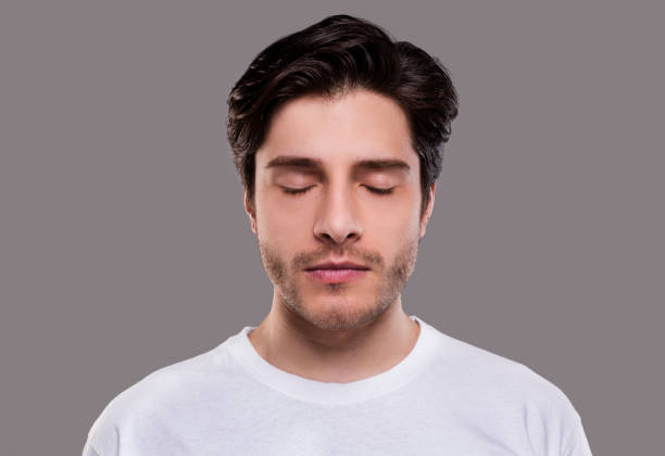 Portrait of handsome millennial man with closed eyes Portrait of handsome millennial man with closed eyes, grey studio background eyes closed stock pictures, royalty-free photos & images