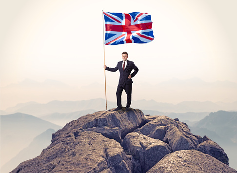 Successful businessman on the top of a mountain holding victory flag