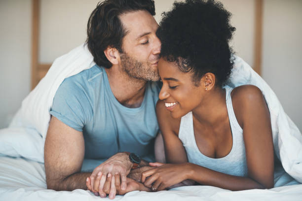 He's completely in love with her Shot of an affectionate middle aged man kissing his wife on her forehead while relaxing on their bed at home forehead photos stock pictures, royalty-free photos & images