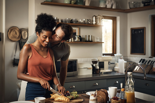 Cropped shot of an affectionate middle aged man kissing his wife on the cheek while she prepares breakfast in their kitchen at home