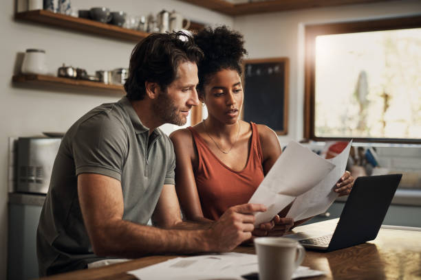 When did this happen? Cropped shot of an affectionate young couple going through paperwork while doing their budget at home black man white woman couple stock pictures, royalty-free photos & images