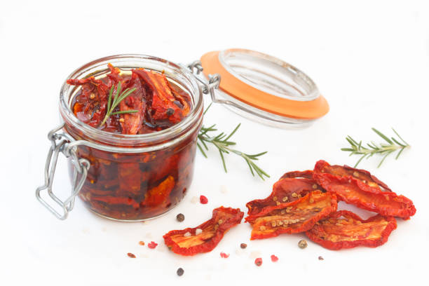 Sun-dried tomatoes with herbs and garlic in glass jar on white background stock photo