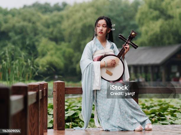 Beautiful Asian Woman In Cyan Costume Clothes Hanfu Holding Yueqin With Lotus Pond Background In Rainy Day Traditional Ancient Chinese Beauty Time Travel Fiction Stock Photo - Download Image Now