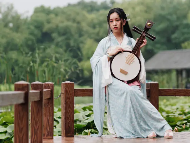 Beautiful Asian woman in cyan costume clothes hanfu holding yueqin (four stringed plucked instrument) with lotus pond background in rainy day, traditional ancient Chinese beauty, time travel fiction.