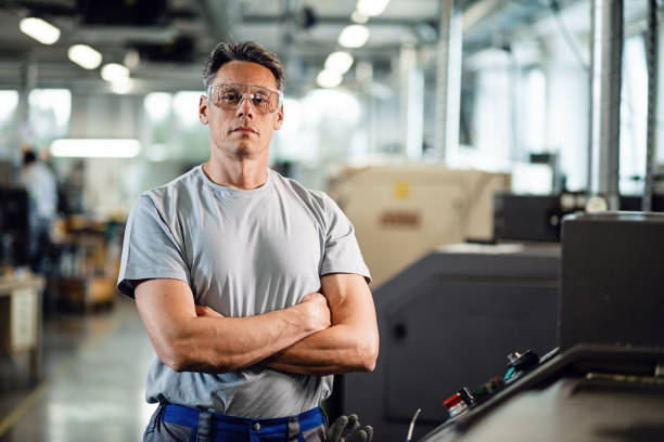 Portrait of confident CNC machine operator in a factory. Portrait of industrial engineer with arms crossed standing by CNC machine and looking at camera. metal worker photos stock pictures, royalty-free photos & images