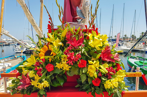 A bouquet of flowers at the foot of the statue of St. Peter the patron saint of seafarers against the background of the fishing port