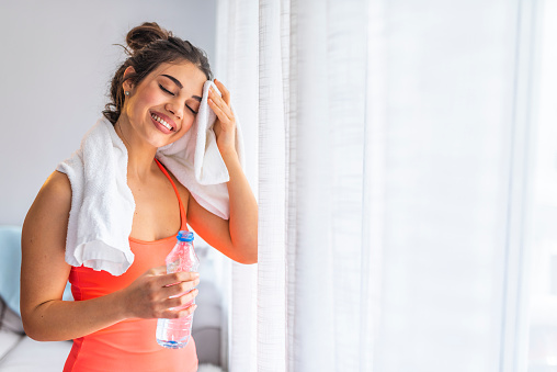 Girl exercising at home she tired and She has sweat on her face. Side profile view photo portrait of sexual attractive beautiful glad sportive woman holding bottle in hand standing in white room