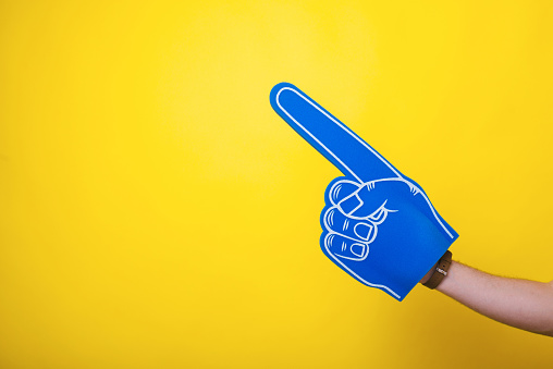 Photo of a handsome arm,  wearing a big blue fan glove, over isolated yellow background
