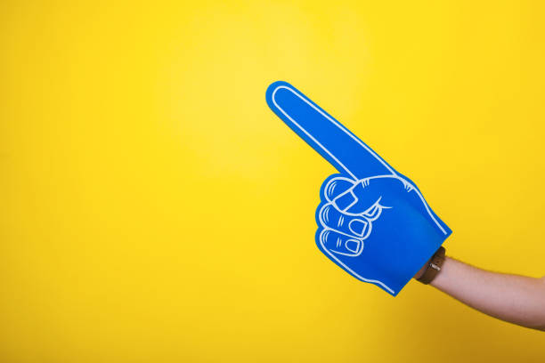 Photo of a handsome arm,  wearing a big blue fan glove, over isolated yellow background stock photo