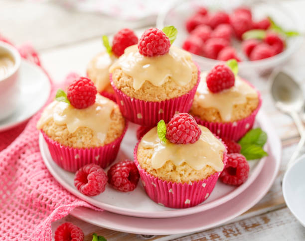 Cupcakes with white chocolate and fresh raspberries on a ceramic plate on a wooden white table, close-up. A delicious dessert or breakfast.