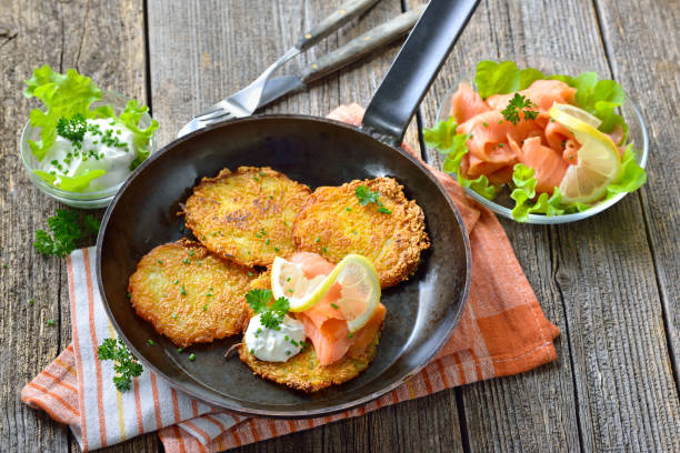 Potato pancakes with salmon Crunchy potato pancakes with smoked salmon and sour cream with fresh green herbs served in an iron frying pan hash brown stock pictures, royalty-free photos & images