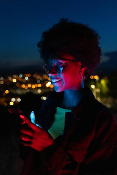 Jeune femme utilisant son téléphone portable la nuit avec la ville à l'arrière-plan - Photo